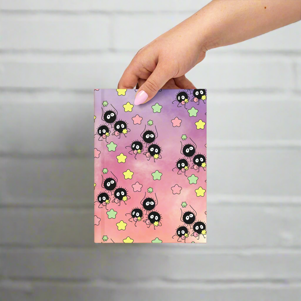 Notebook with a colorful design of black characters and stars held by a hand on a white background