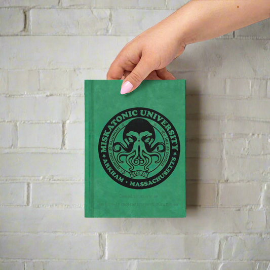 Green notebook with 'Miskatonic University' logo held by a hand on a white background